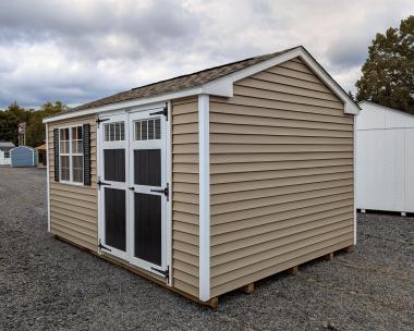 10x14 peak series shed in pebble clay straight lap vinyl siding with white trim and corners, black shutters and door, and weatherwood shingles.